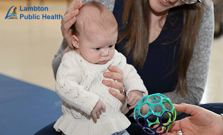 Baby wearing white sweater playing with a ball.