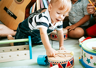 Child reaching for a drum with other instruments behind them.