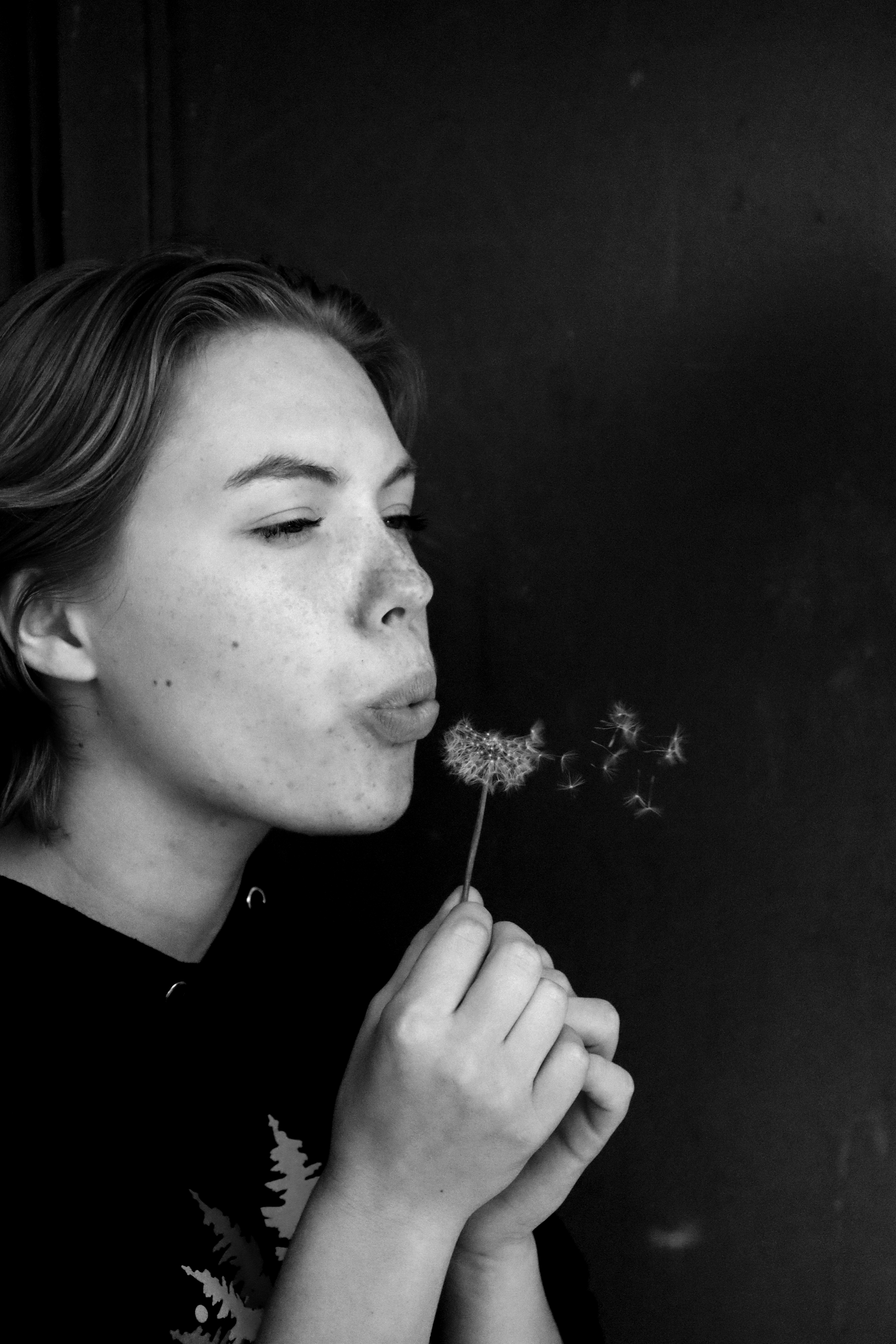 black and white photo of woman blowing dandelion fluff