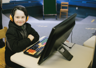 Child with headphones on sitting at a desktop computer.