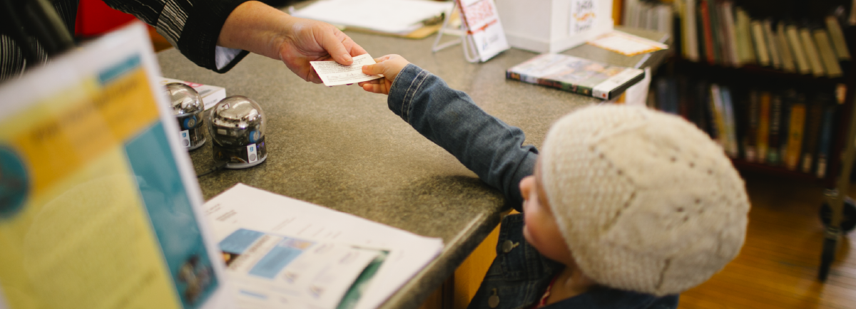 Girl handing her library card to library staff.