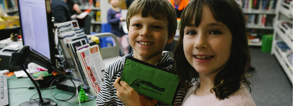 Two kids holding a Lambton County Library branded tote bag.