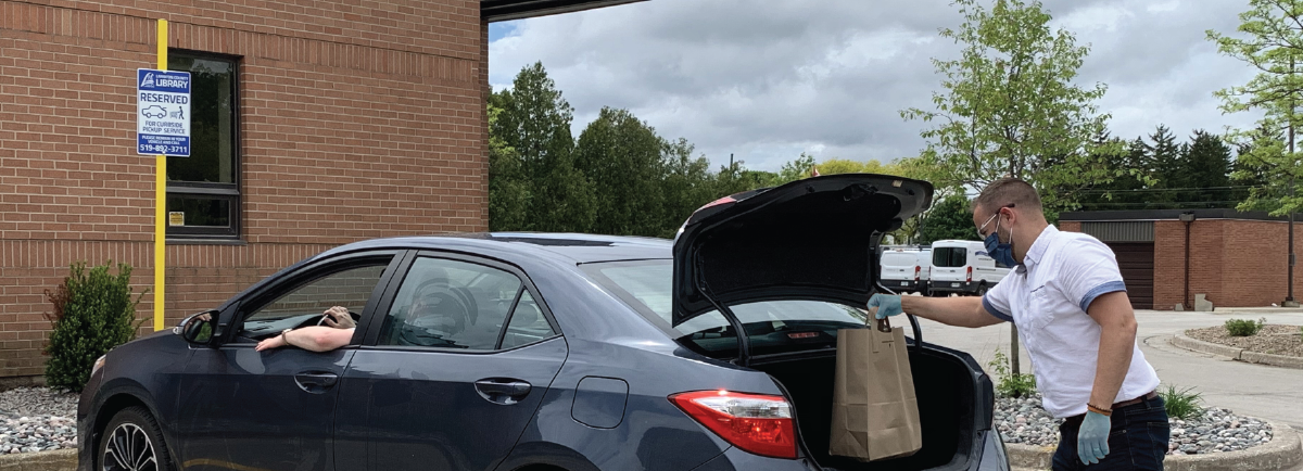 Library staff putting books in trunk of car.