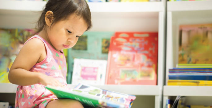 Young girl sitting in a library, reading a book.