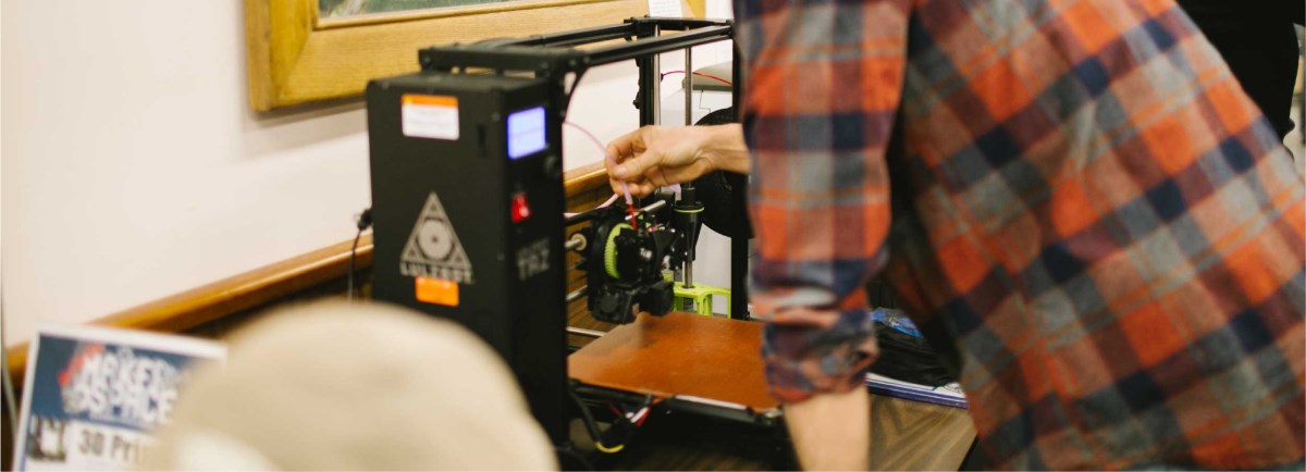 Man using 3D Printer that is on a table.