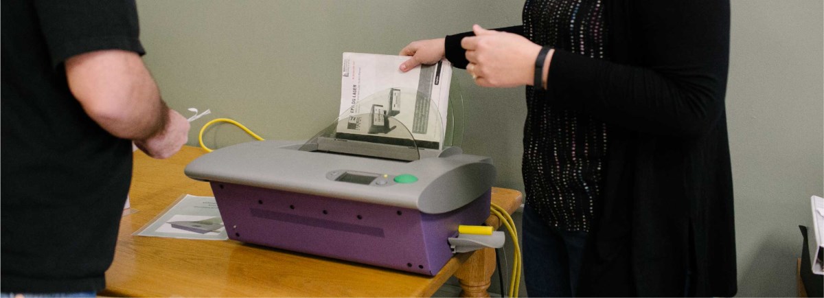 Woman putting paper in a book binder on a table. 