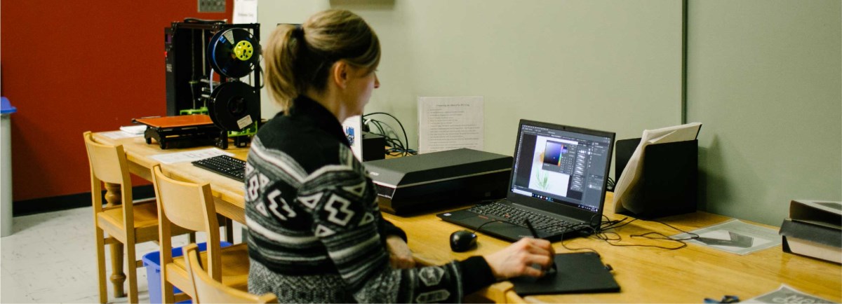 Women sitting at table with laptop and 3D Printer.