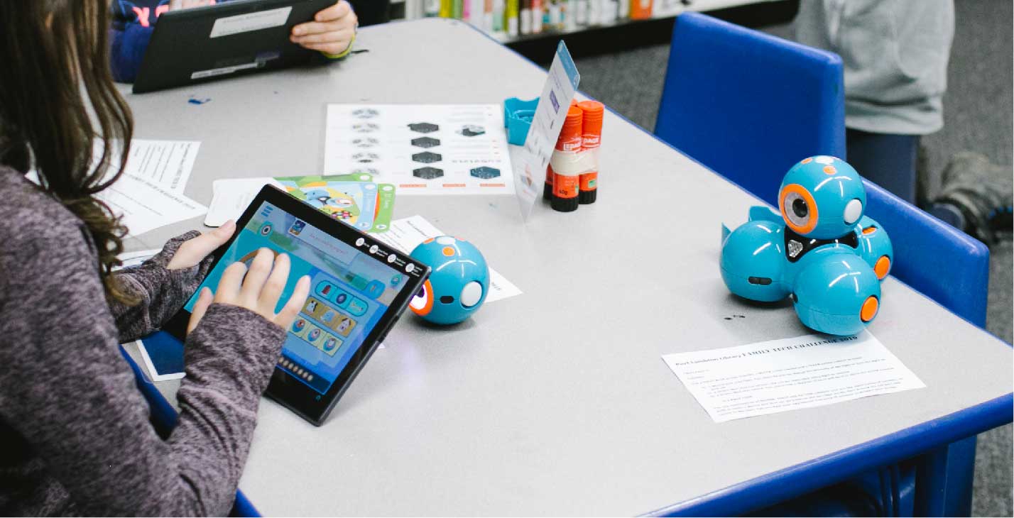 Blue robot sitting on table with tablet.