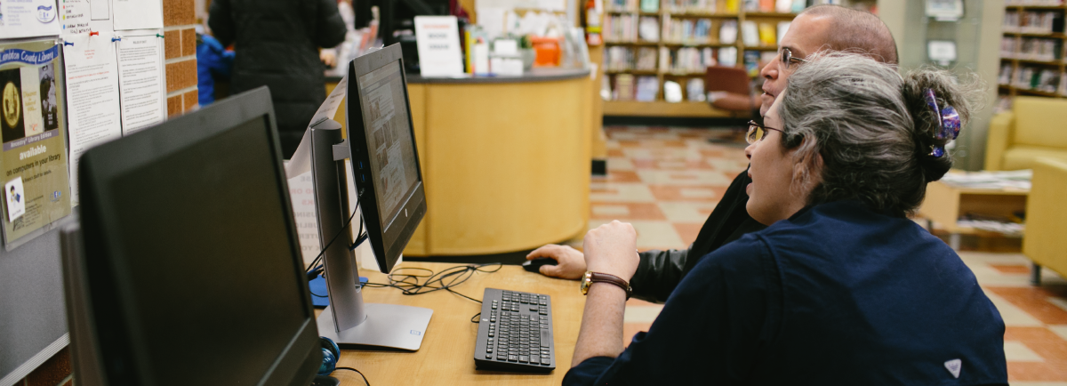 Woman tutoring man at a computer.