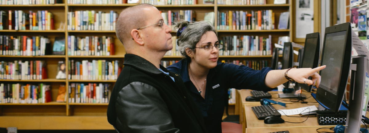 Library staff member pointing at the computer as a man watches.