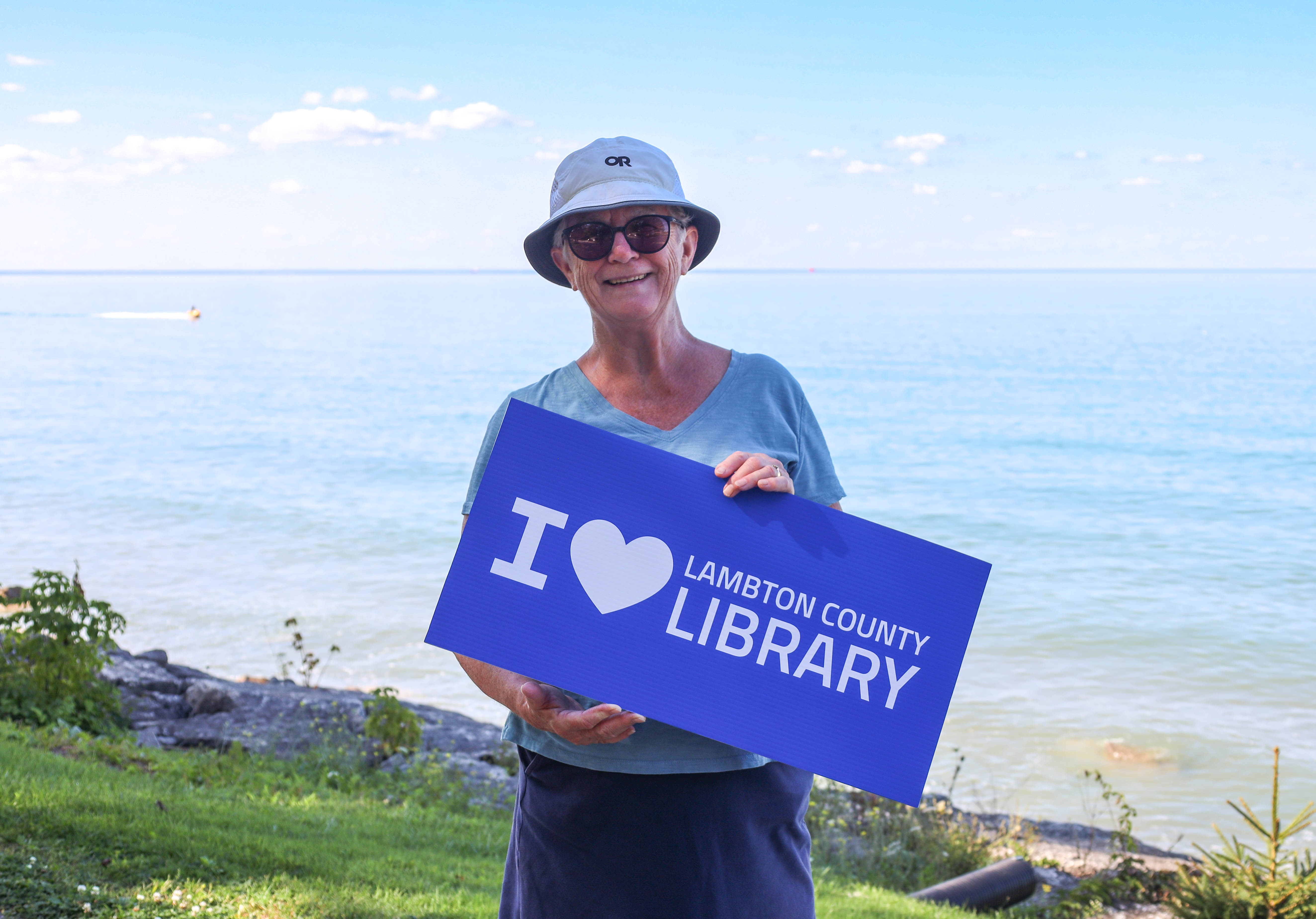 Gwen Moore, a library patron, holds an 'I Love Lambton County Library' sign at Bright's Grove