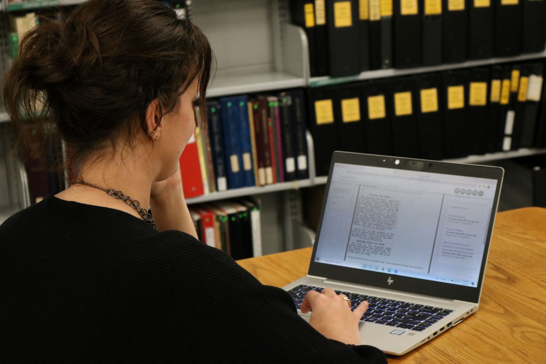 White woman with brown hair is using her laptop to research historical newspapers. 