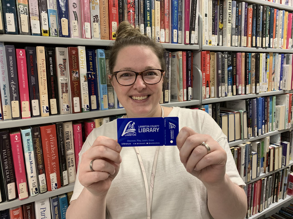 White lady holding up a blue card in front of a shelf of books.