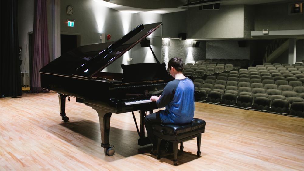 Child at piano on a stage.