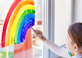 Child painting a rainbow on a window.