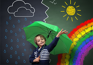 A boy in front of a chalkboard with different weather events drawn on it: rainbow, raining, sunny, etc.