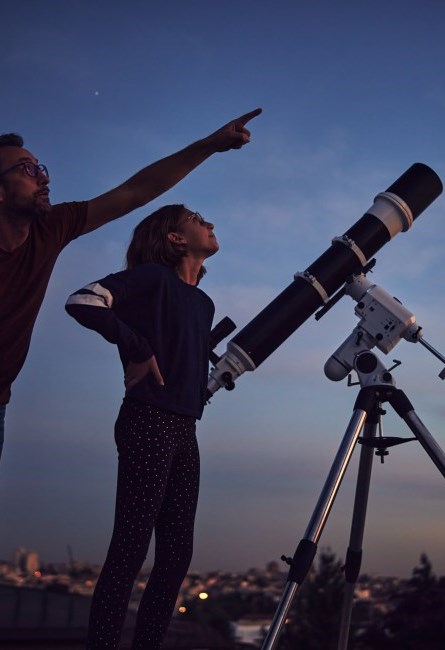 Man pointing in the night sky with a child standing next to a telescope.