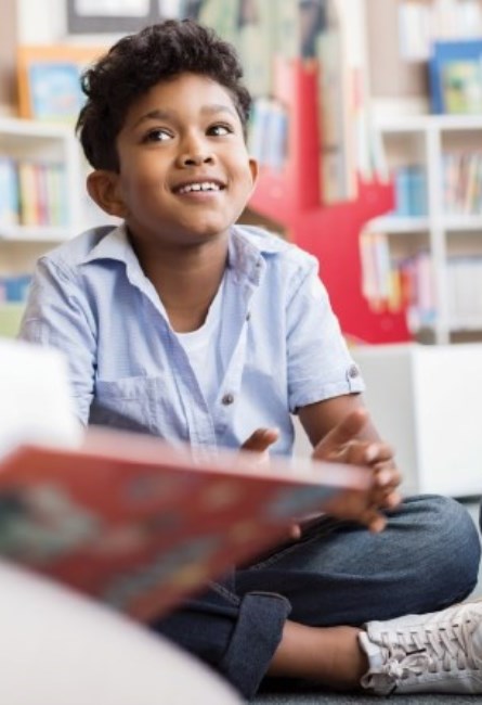 Boy sitting on a carpet in a library.