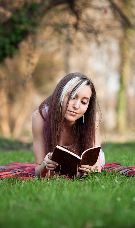 White girl laying in the grass reading a book.