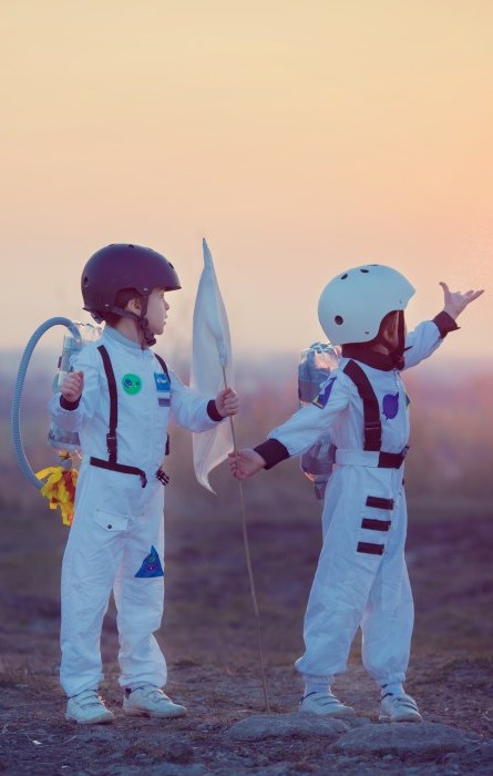 Two little boys standing outside in astronaut outfits.