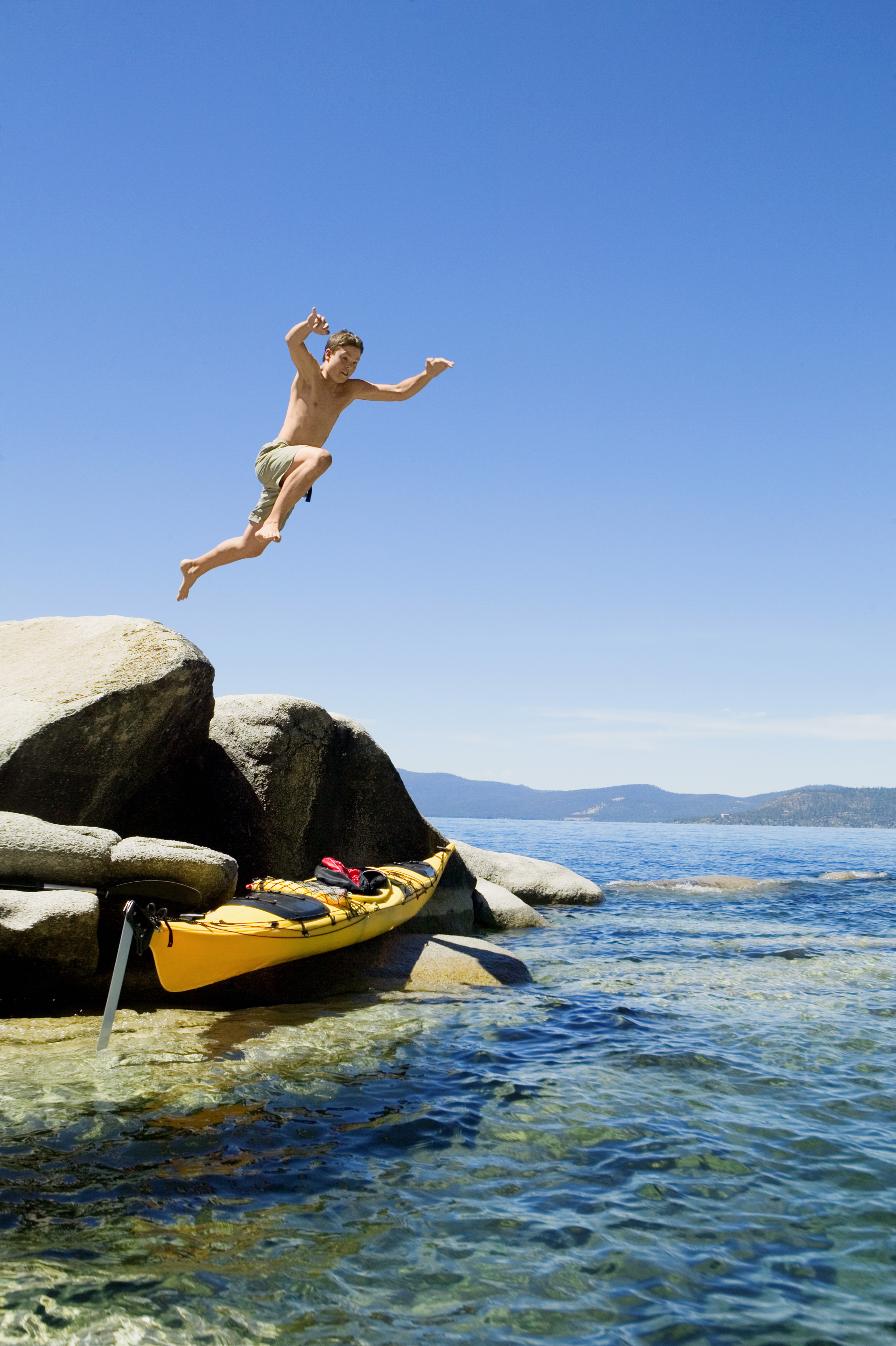 Teenage boy jumping from rocks into water