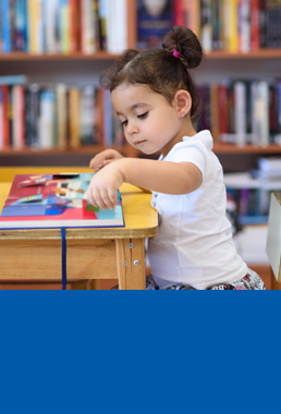 Child sitting at a table looking at a book.