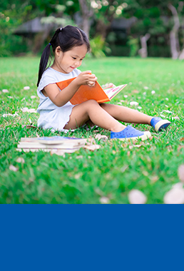 Little girl sitting in grass reading a book.