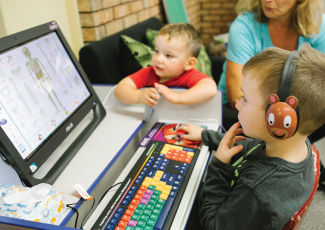 Two children sitting around a computer. 