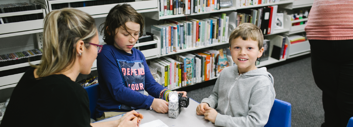 Children and teacher sitting around a table using robots. 